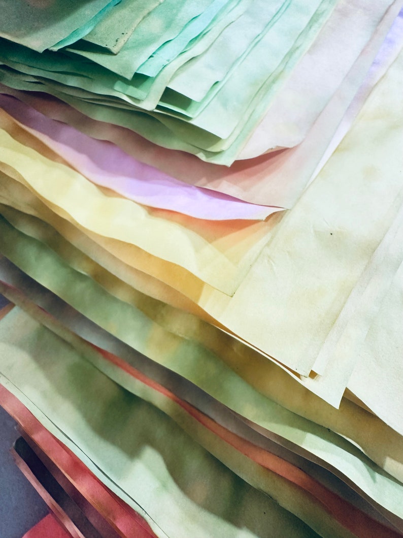 May include: A stack of colorful paper sheets in various shades of green, yellow, pink, and white. The paper is slightly textured and has a vintage look.