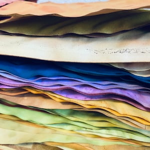 May include: A stack of colorful, textured paper sheets in various shades of blue, purple, yellow, green, and brown. The paper is layered and slightly wavy, creating a visually appealing and artistic effect.