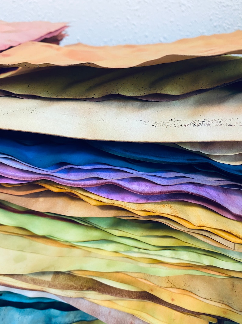 May include: A stack of colorful, textured paper sheets in various shades of blue, purple, yellow, green, and brown. The paper is layered and slightly wavy, creating a visually appealing and artistic effect.