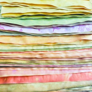 May include: A stack of colorful fabric strips in shades of yellow, green, orange, pink, and purple. The fabric is arranged in a layered pattern, creating a visually appealing and textured display.