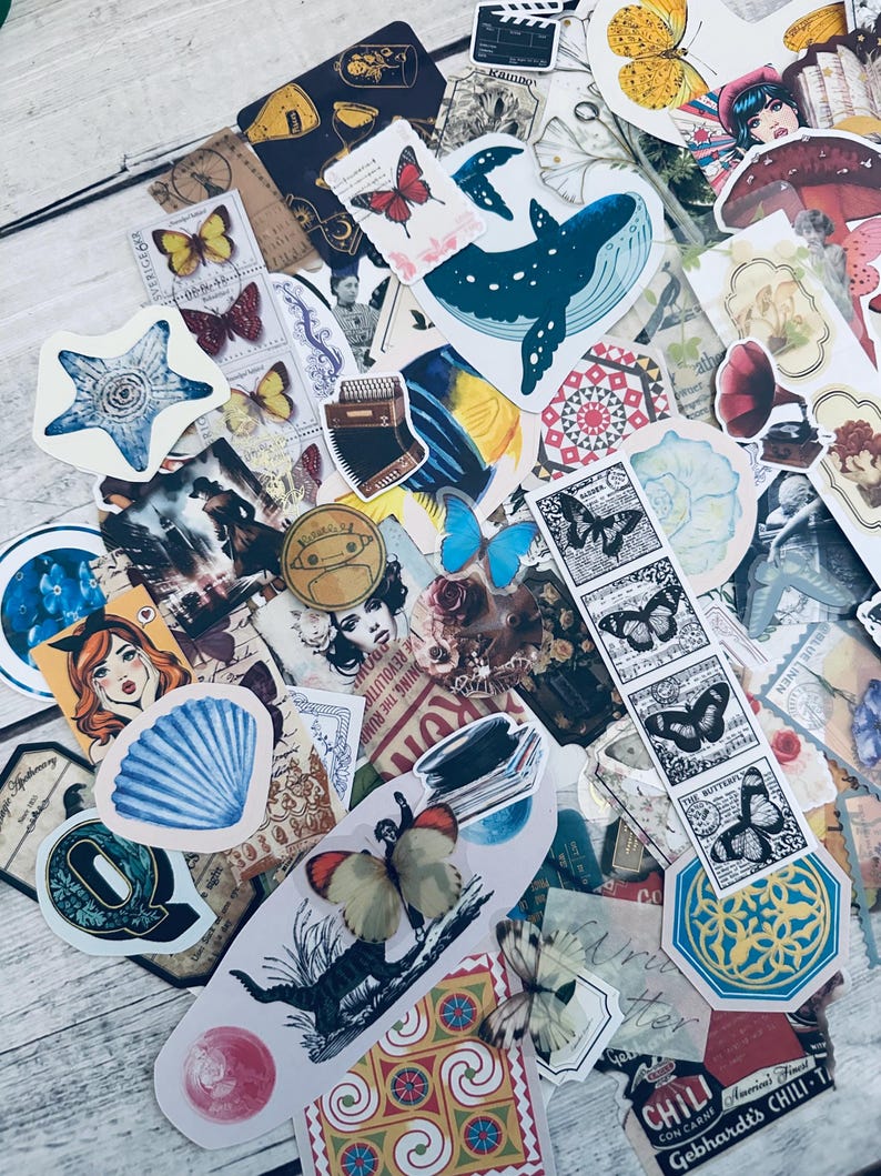 May include: A collection of colorful vintage-style stickers featuring butterflies, flowers, a whale, a seashell, a star, and other designs. The stickers are on a white wooden surface.