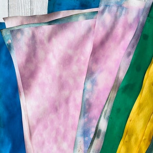 May include: A stack of fabric scraps in various shades of blue, green, yellow, and pink. The fabric is folded and layered, creating a colorful and textured display.