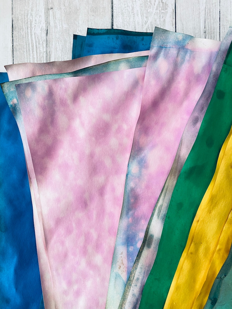 May include: A stack of fabric scraps in various shades of blue, green, yellow, and pink. The fabric is folded and layered, creating a colorful and textured display.