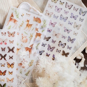 May include: Three sheets of clear sticker paper with various designs. One sheet features a variety of butterflies in shades of purple, blue, and white. Another sheet features a variety of deer in shades of brown and white. The third sheet features a variety of butterflies in shades of brown, white, and black.