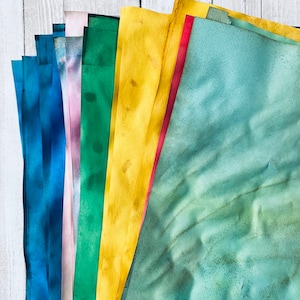 May include: A stack of colorful paper sheets in shades of blue, purple, green, yellow, and red. The paper is textured and has a watercolor effect.