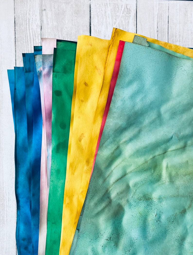May include: A stack of colorful paper sheets in shades of blue, purple, green, yellow, and red. The paper is textured and has a watercolor effect.