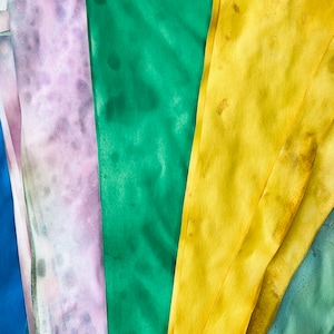 May include: Five fabric swatches in different colors and patterns. The swatches are arranged in a fan shape. The colors are purple, green, yellow, blue, and green.