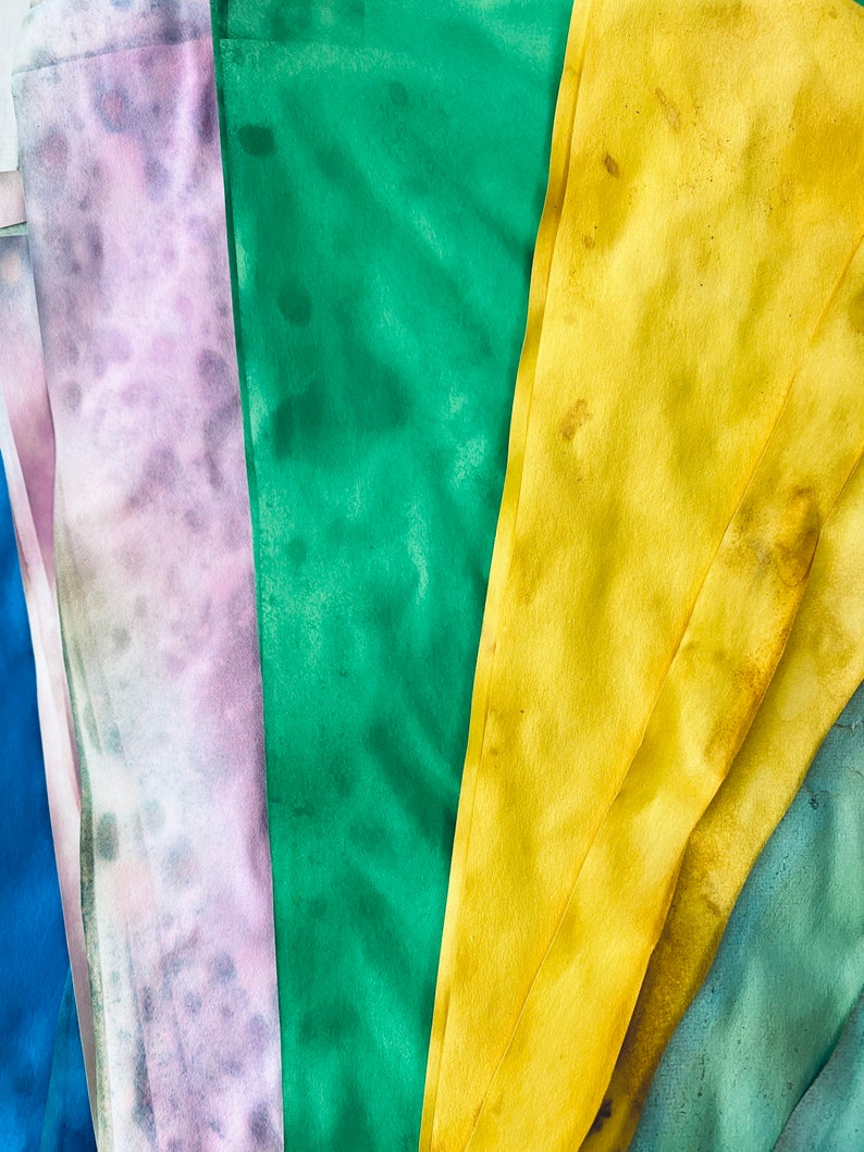 May include: Five fabric swatches in different colors and patterns. The swatches are arranged in a fan shape. The colors are purple, green, yellow, blue, and green.