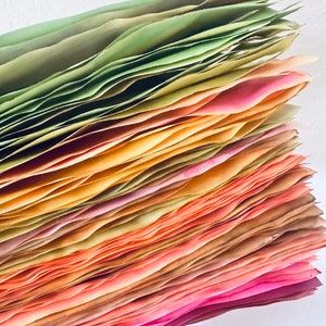 May include: A stack of colorful tissue paper in shades of green, yellow, orange, pink, and red. The paper is folded and layered, creating a gradient effect.