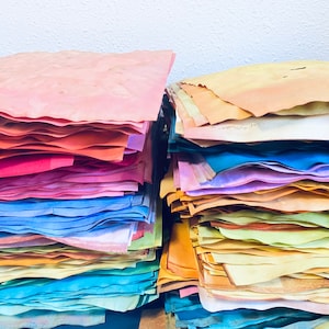May include: A stack of colorful handmade paper sheets in various shades of pink, red, blue, yellow, and green. The paper is arranged in a rainbow pattern.
