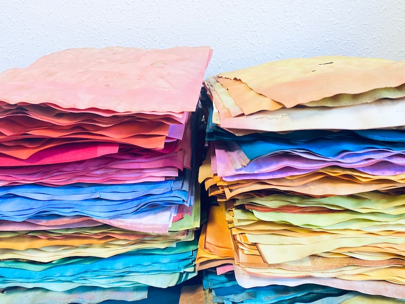 May include: A stack of colorful handmade paper sheets in various shades of pink, red, blue, yellow, and green. The paper is arranged in a rainbow pattern.