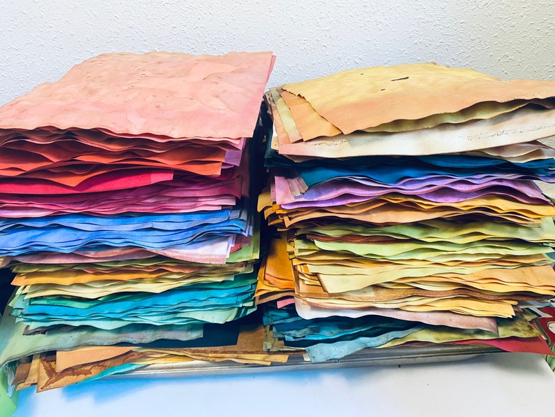 May include: A stack of colorful handmade paper sheets in various shades of blue, green, yellow, orange, red, and brown. The paper is arranged in a rainbow pattern.