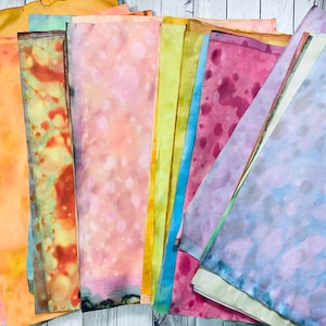 May include: A collection of 10 hand-dyed fabric squares in various shades of yellow, orange, pink, red, blue, and green. The fabric has a mottled, watercolor-like appearance.