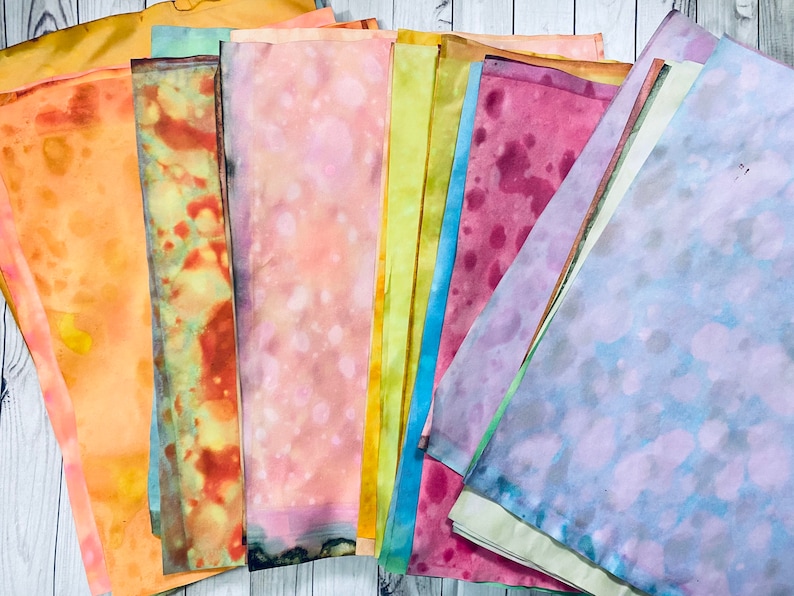 May include: A collection of 10 hand-dyed fabric squares in various shades of yellow, orange, pink, red, blue, and green. The fabric has a mottled, watercolor-like appearance.