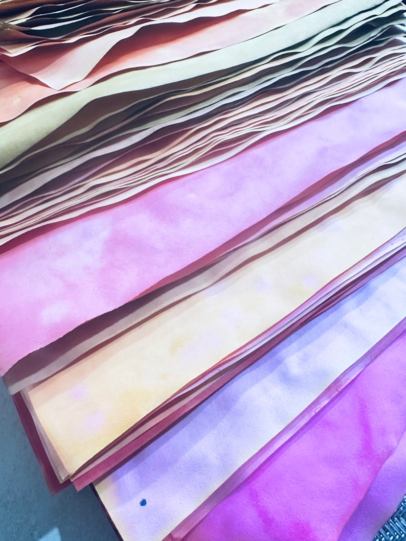 May include: A stack of colorful paper sheets in shades of pink, yellow, and orange. The paper is layered and folded, creating a textured and abstract pattern.