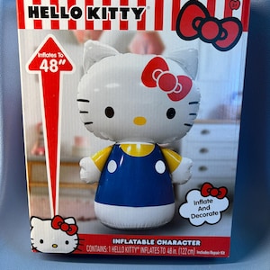 May include: A Hello Kitty inflatable character in a box. The packaging features red and white stripes, a red bow, and text stating it inflates to 48 inches. The character is white with a yellow nose, black eyes, and a blue dress with yellow sleeves.