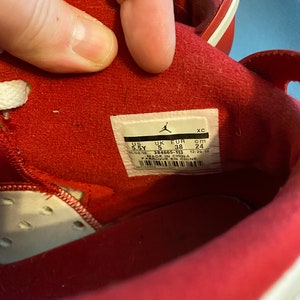 May include: Close-up of the inside of a red shoe with a white label that reads "UK EUR cm 5 38 24 11/02/16 384665-113 12/29/16 MADE IN CHINA FABRIQUE EN CHINE".