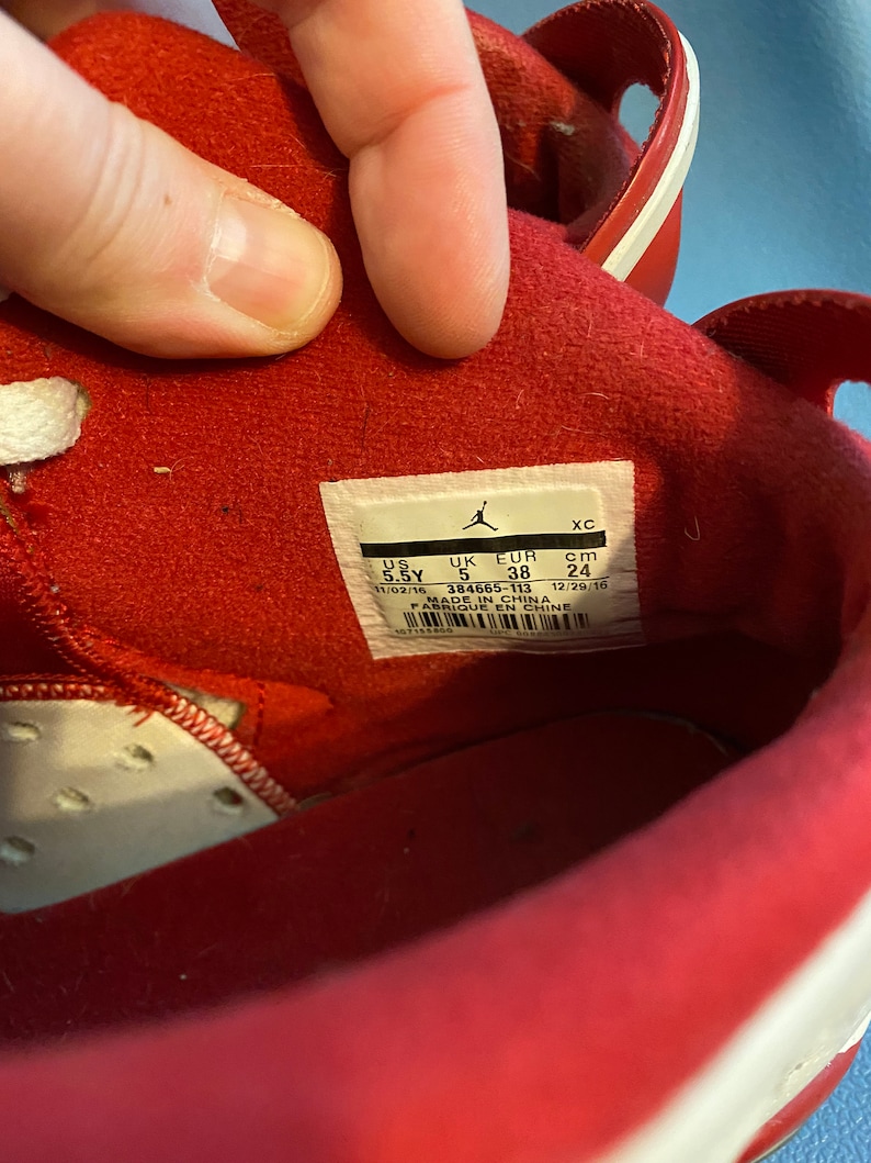 May include: Close-up of the inside of a red shoe with a white label that reads "UK EUR cm 5 38 24 11/02/16 384665-113 12/29/16 MADE IN CHINA FABRIQUE EN CHINE".