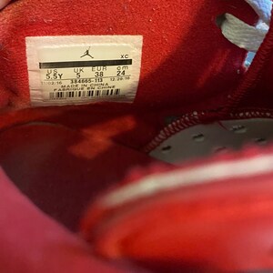 May include: A red shoe size tag with the text "US 5.5Y UK 5 EUR 38 cm 24 11/02/16 384665-113 MADE IN CHINA FABRIQUE EN CHINE 12/29/16"