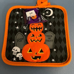 Puede incluir: Manopla de cocina con temática de Halloween, con ribete y lazo naranja. El diseño presenta una pila de tres calabazas naranjas, lápidas, calaveras, estrellas y una araña sobre un fondo negro con estampado de diamantes. Mide 17,5 cm x 17,5 cm.