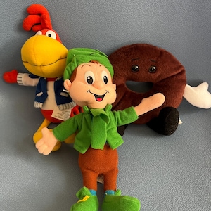 May include: Three plush toys: a red and yellow rooster, a green leprechaun, and a brown donut with a face.