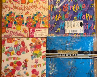 Puede incluir: Cuatro paquetes de papel de regalo plegados. Arriba a la izquierda: patrón floral con texto 'Happy Birthday'. Arriba a la derecha: patrón de cuadros azules con 'Happy Birthday' y notas musicales. Abajo a la izquierda: tren y animales. Abajo a la derecha: azul con notas musicales.