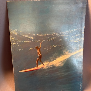 May include: Vintage print of a surfer riding a wave. The surfer is standing on a red and white surfboard, with the ocean in the background. The image has a retro aesthetic.