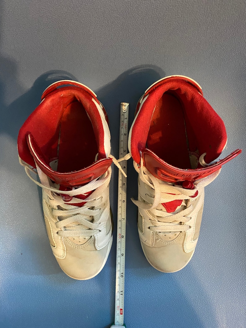 May include: A pair of white and red high-top sneakers with white laces. The sneakers are on a blue surface with a ruler for scale.