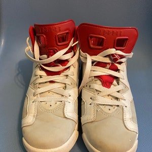 May include: A pair of white and red sneakers with white laces. The sneakers have the text "JORDAN" on the back of the shoe.