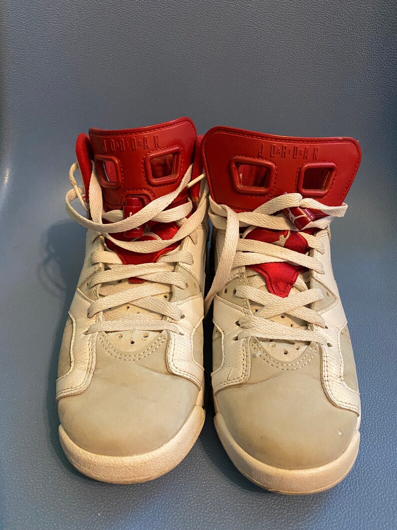 May include: A pair of white and red sneakers with white laces. The sneakers have the text "JORDAN" on the back of the shoe.