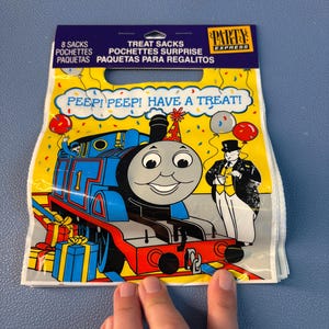 May include: A pack of 8 Party Express treat sacks featuring a blue Thomas the Tank Engine train wearing a party hat, Sir Topham Hatt, and colorful balloons. The yellow background includes confetti and the text PEEP! PEEP! HAVE A TREAT!