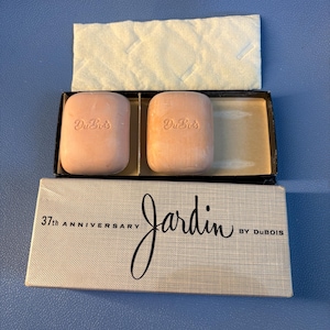May include: A vintage Jardin by Dubois soap set. The set includes two pink bars of soap in a black box with a white quilted liner. The box reads "37th Anniversary Jardin by Dubois."