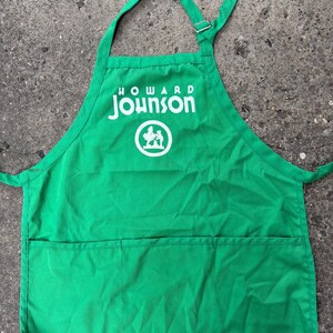 May include: A bright green apron with the "Howard Johnson" logo in white. The apron has a large front pocket and an adjustable neck strap with a metal buckle. The logo features the name and a circular graphic.