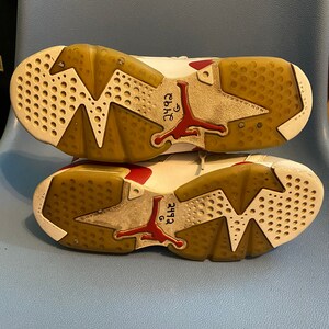 May include: A pair of white and red sneakers with a brown sole. The sneakers have a red Jumpman logo on the side and the text "6" and "23" written on the sole.