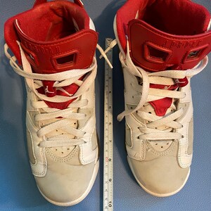May include: A pair of white and red sneakers with white laces. The sneakers have a red tongue and a red back tab. The sneakers are on a blue surface.