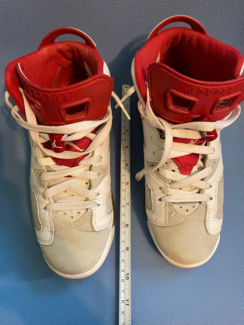 May include: A pair of white and red sneakers with white laces. The sneakers have a red tongue and a red back tab. The sneakers are on a blue surface.