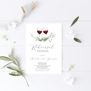 Puede incluir: Una invitación a una cena de ensayo de boda con una ilustración de acuarela de dos copas de vino con vino tinto y hojas verdes. El texto dice "Cena de ensayo en honor de Amanda y Brandon" con la fecha, la hora y la ubicación del evento.