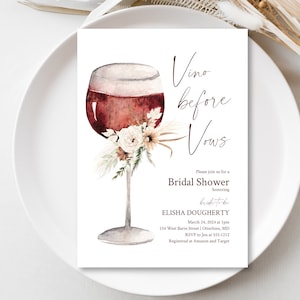 Puede incluir: Una tarjeta de invitación a una despedida de soltera con una ilustración en acuarela de una copa de vino tinto adornada con flores. El texto "Vino before Vows" está escrito en una elegante escritura, con detalles del evento debajo.