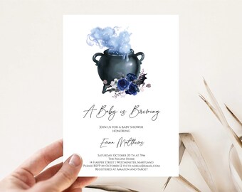 May include: Baby shower invitation featuring a dark blue cauldron with blue smoke and floral accents. The text "A Baby is Brewing" is displayed in elegant script, along with event details. A perfect announcement for a baby shower.