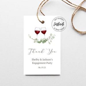 Puede incluir: Etiqueta de regalo blanca con dos copas de vino tinto, follaje verde y la frase "Thank You". El texto incluye "Shelby & Jackson's Engagement Party" y la fecha 06.19.21. Una cuerda marrón está adjunta.