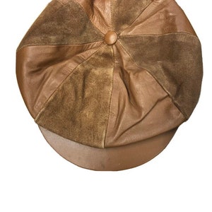 May include: A brown leather newsboy cap with a rounded crown and a short, curved brim. The cap features a button at the centre and is constructed from panels of smooth and suede-like leather. A classic hat for any wardrobe.