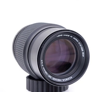 May include: A black Konica Hexar AF 135mm f2.8 lens with the text "KONICA HEXAR AF 135mm f2.8 LENS MADE IN JAPAN 4191229 858" printed on the side.