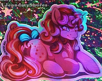 May include: Two holographic stickers featuring cartoon ponies. One pony has a green and purple body with a pink and purple mane. The other pony is pink with a red mane and a blue bow. Text at the top reads "Sold Only @ L'Jendary Shores".