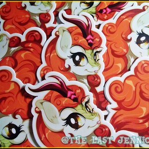 May include: A collection of stickers featuring a cartoon character with orange hair, a white face, and large brown eyes. The character has a green and white face with a horn. The stickers are scattered across a surface. The text "@THE LAST JENNICORN" is visible.