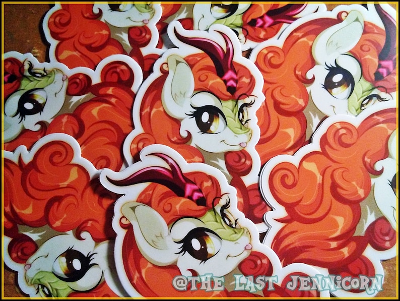 May include: A collection of stickers featuring a cartoon character with orange hair, a white face, and large brown eyes. The character has a green and white face with a horn. The stickers are scattered across a surface. The text "@THE LAST JENNICORN" is visible.
