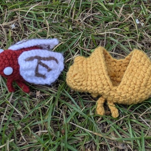 May include: A red and white crocheted insect with brown text on the wings, and a yellow crocheted hooded garment.