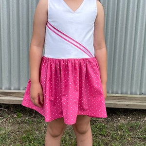 May include: A white sleeveless dress with a pink diagonal stripe and a pink polka dot skirt.