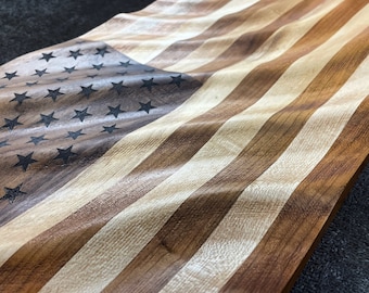 May include: A wooden American flag with a wavy design. The flag is made of different types of wood, creating a unique and rustic look. The stars are black and the stripes are red, white, and blue.