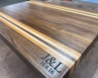 May include: A rectangular wooden cutting board with a walnut finish and two maple stripes. The board is engraved with "J&L 10.8.16".
