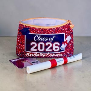 May include: A red and white glittery graduation-themed pouch with the text "Class of 2026" and a diploma. A graduation cap is also visible. A small card and a diploma are in front of the pouch.
